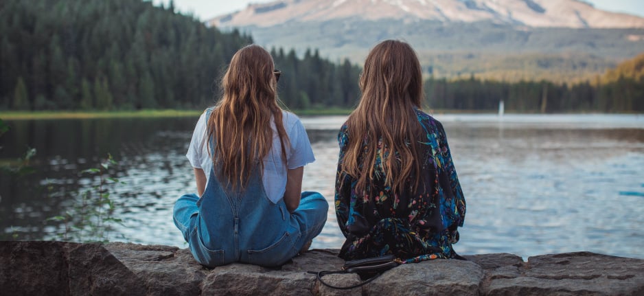 two girls sitting by lake